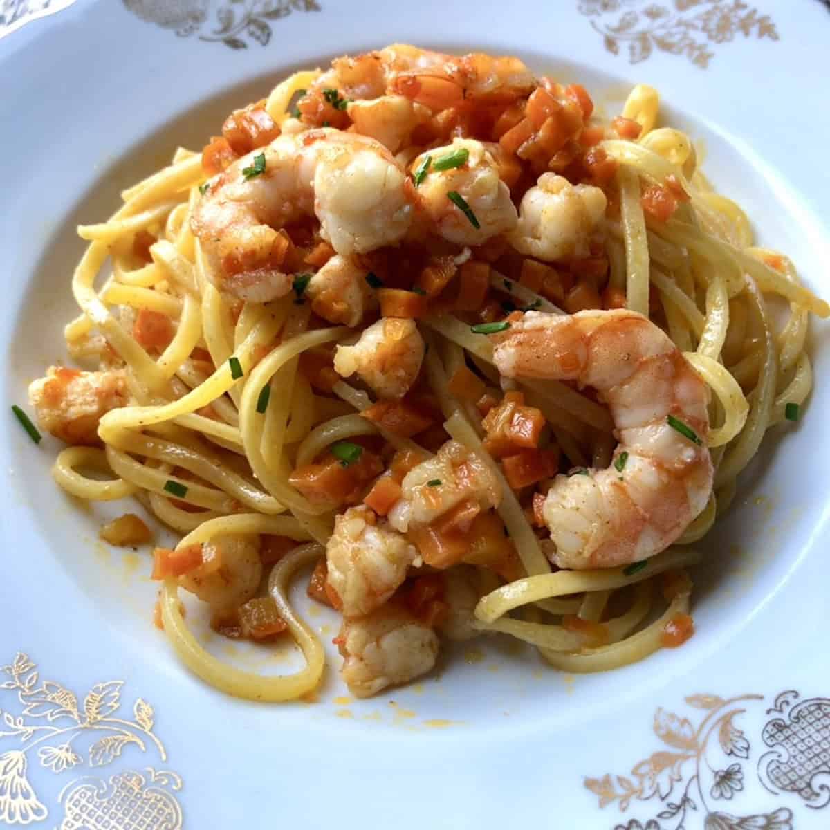 A bowl of homemade shrimp and carrot pasta alla chitarra, spaghetti alla chitarra recipe with seafood served in a pasta bowl.
