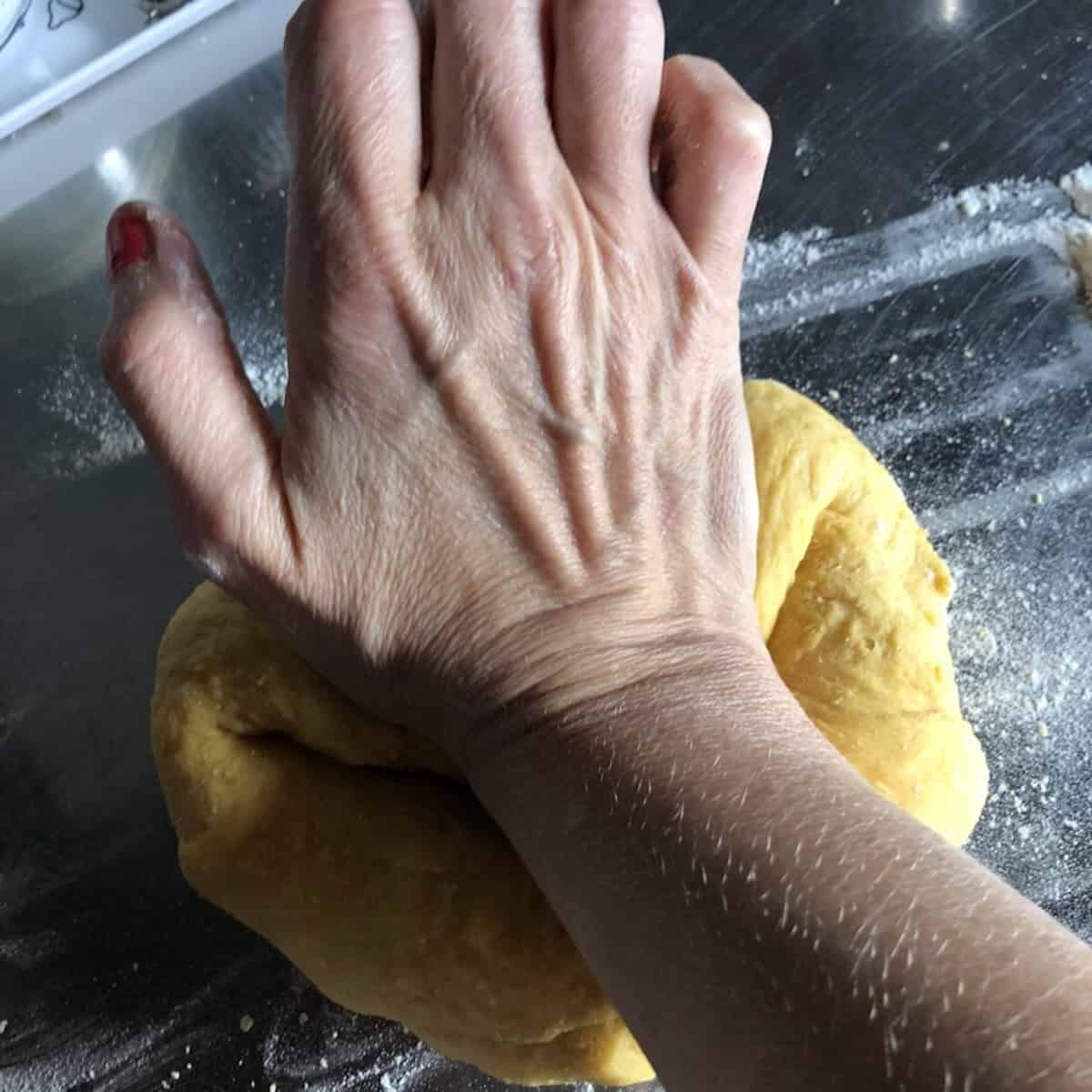 Hand kneading semolina egg chitarra pasta dough on a lightly floured countertop, maccheroni alla chitarra dough from scratch.