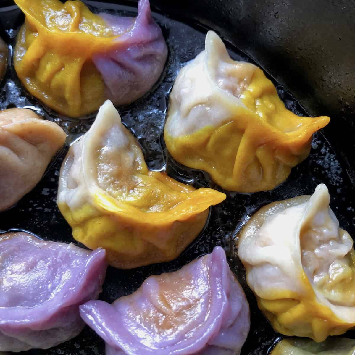 Closeup of Mardi Gras colored Chinese potstickers after cooking showing naturally colored gold turmeric and white, gold and purple cabbage dumpling wrappers for homemade dumplings recipe.
