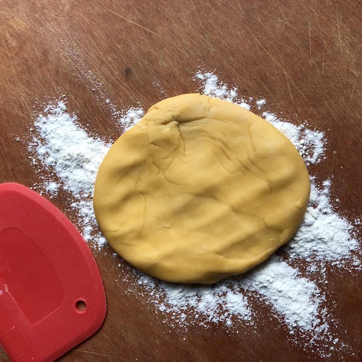 A portioned piece of chitarra pasta dough floured and ready to roll to thickness before cutting on the chitarra tool.
