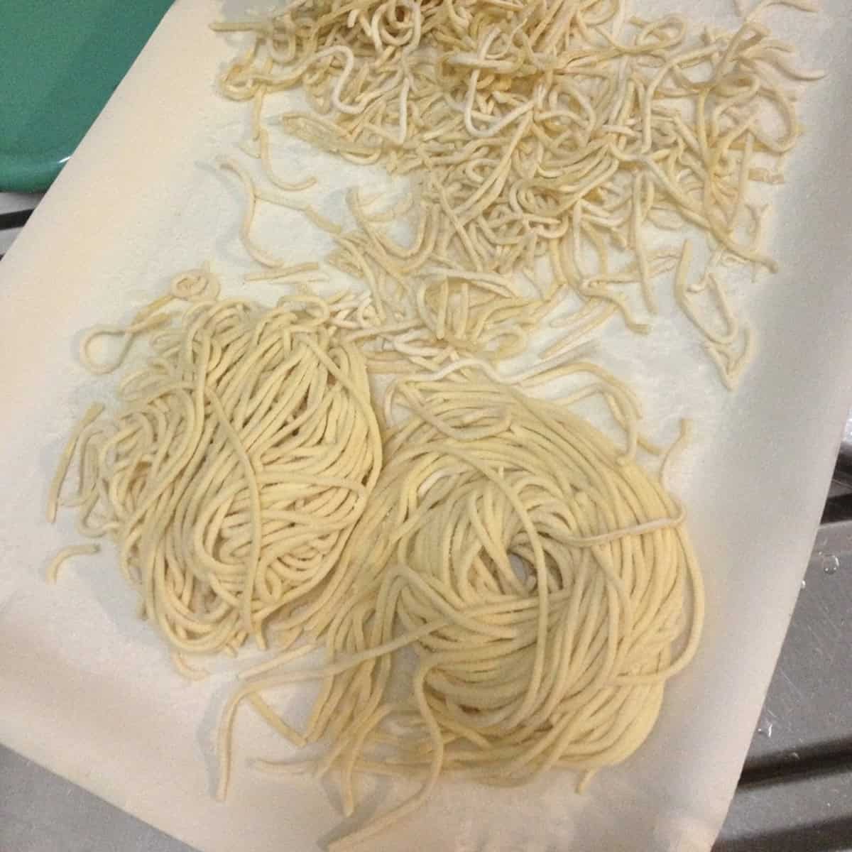 Zia Linda's homemade spaghetti alla chitarra twirled into nests on a paper tray ready to cook or freeze, chitarra pasta recipe made from scratch in Abruzzo Italy.
