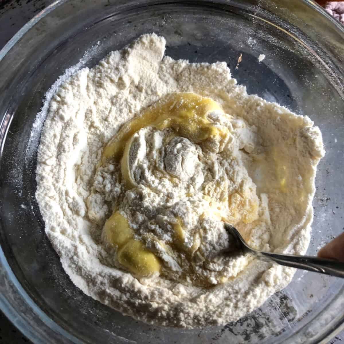 Stirring the eggs into the semolina flour with a fork, spaghetti alla chitarra recipe mixing step.
