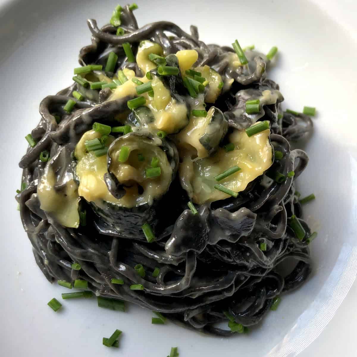 Black spaghetti alla chitarra with creamy zucchini alfredo sauce in pasta bowl, homemade squid ink noodles with make-ahead white sauce recipe.