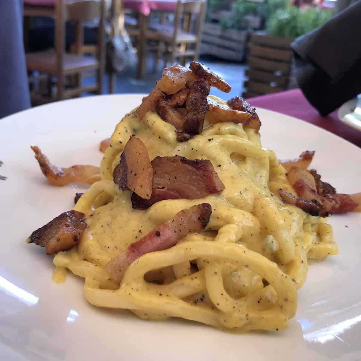 A plate of thick square-cut tonnarelli chitarra pasta in creamy carbonara sauce topped with crispy guanciale strips and cracked black pepper, aka tonnarelli the Roman version of Abruzzo's chitarra pasta.
