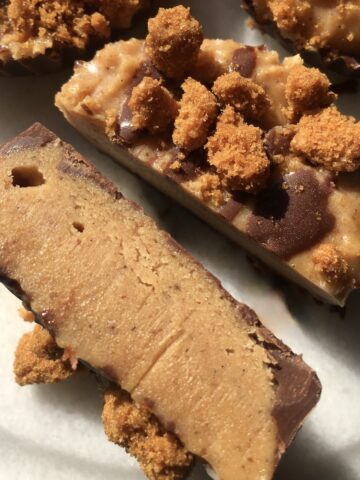 A peanut butter cup with biscoff cookies and chocolate sliced in half to show the middle layer with more whole cups in the background.
