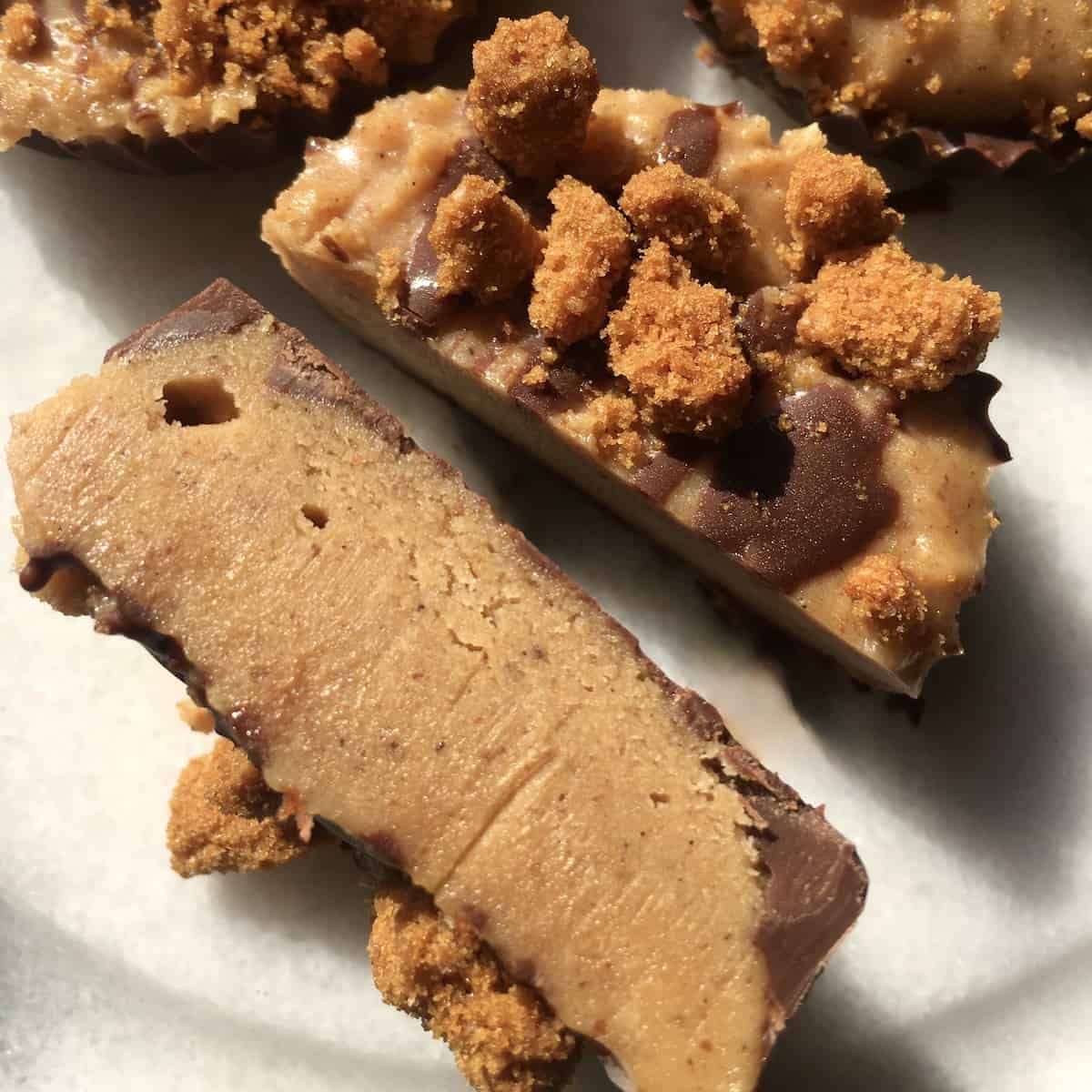 A peanut butter cup with biscoff cookies and chocolate sliced in half to show the middle layer with more whole cups in the background.