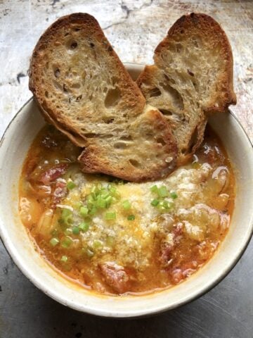 A bowl of homemade Italian ventricina and cicerchia bean soup garnished with grated parmesan and scallions and two parmesan crostini.