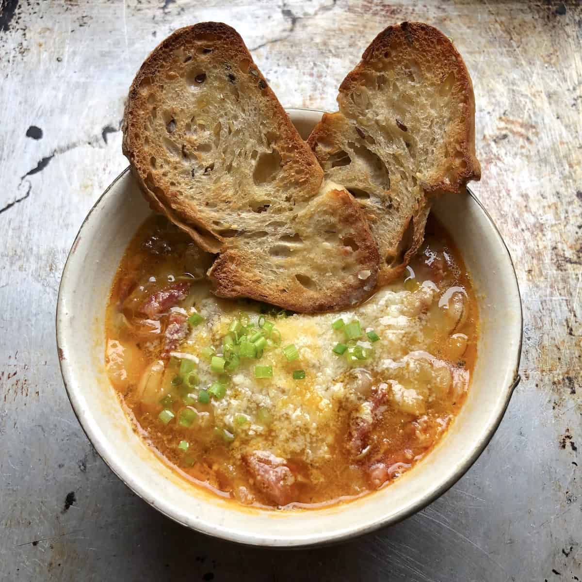 A bowl of homemade Italian ventricina and cicerchia bean soup garnished with grated parmesan and scallions and two parmesan crostini.