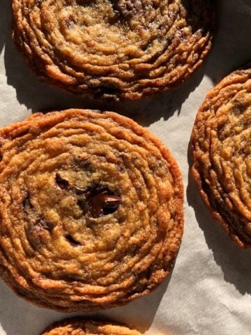 Oversized bakery-style pan-banging chocolate chip cookies on a parchment-lined half-sheet baking pan.
