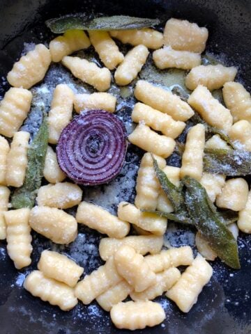 Cast iron skillet gnocchi with sage, olive oil, and parmesan cheese with seared caramelized purple onion.