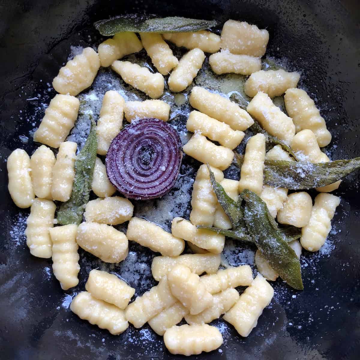 Cast iron skillet gnocchi with sage, olive oil, and parmesan cheese with seared caramelized purple onion.