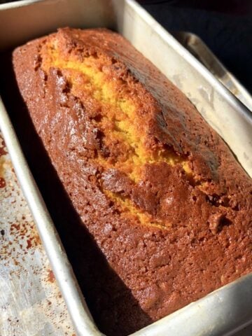 A loaf of cooling pumpkin bread loaf glistening with a bakery-style crevice down the middle.