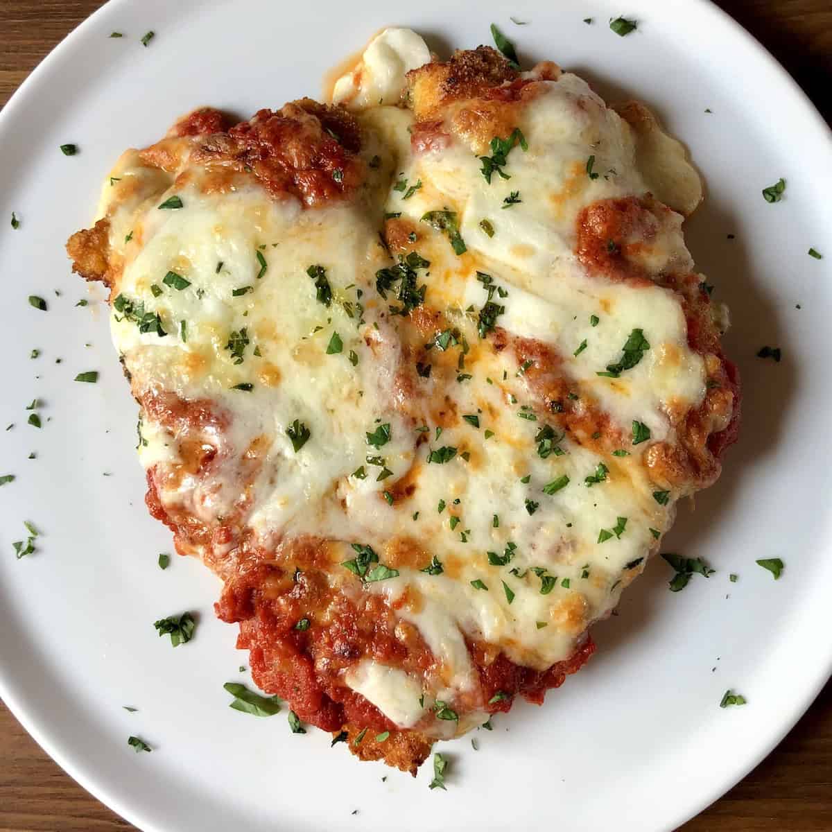 A top down view of a huge full chicken breast panko-crusted chicken parmesan (chicken parmigiana) on a plate.