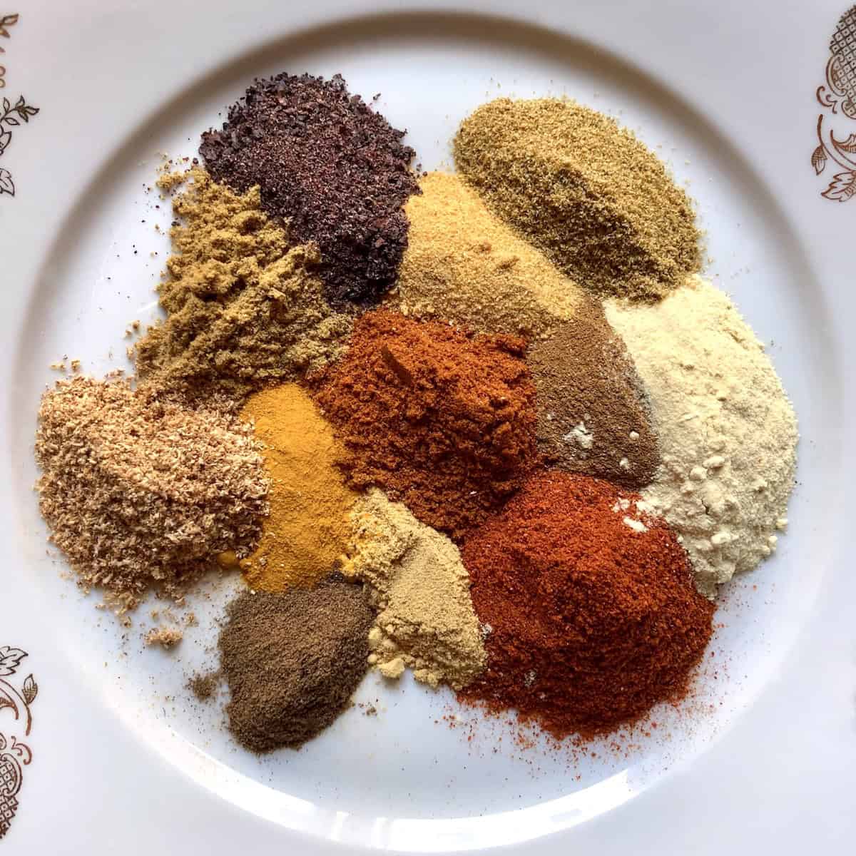 A plate filled homemade shawarma seasoning with 12 small individual mounds of spices that make it up.