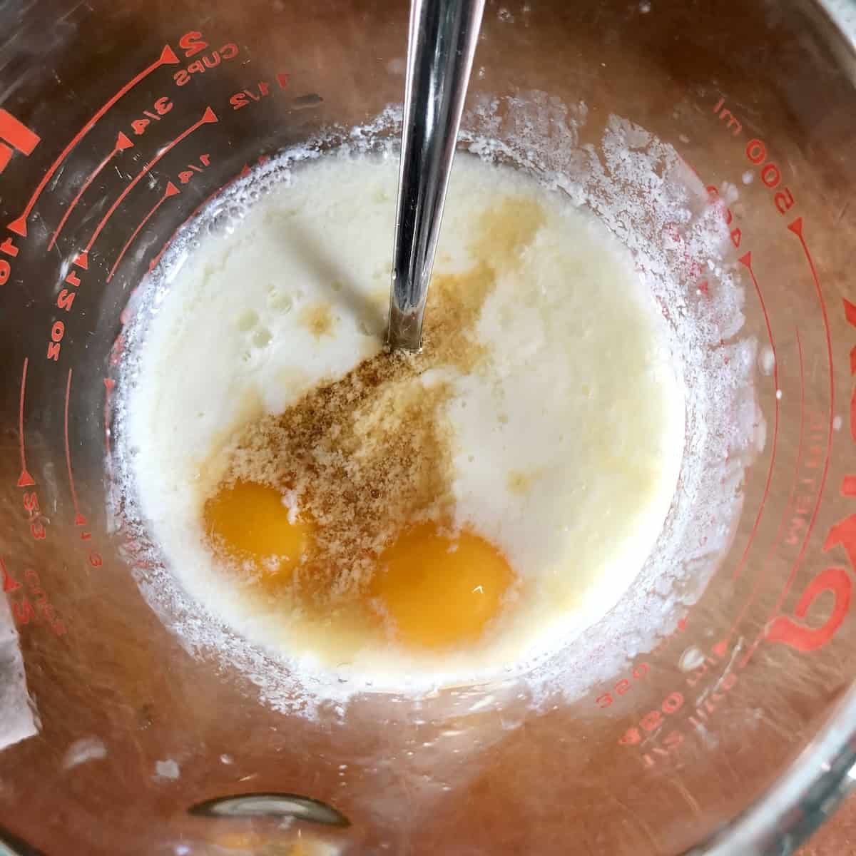 Wet pancake ingredients for pumpkin pancakes recipe with pumpkin puree, buttermilk, egg yolks and vanilla in glass measuring cup for making easy buttermilk pumpkin pancakes from scratch.