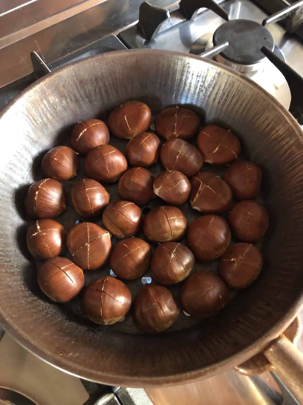 Scored chestnuts roasting in traditional Italian chestnut pan with holes for topping pumpkin pancakes recipe showing unique topping for the best pumpkin pancakes from scratch.