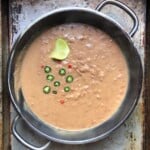 A saute pan with the creamiest refried beans garnished with a a few sliced fresh jalapeños, chili pequin, and a lime wedge.