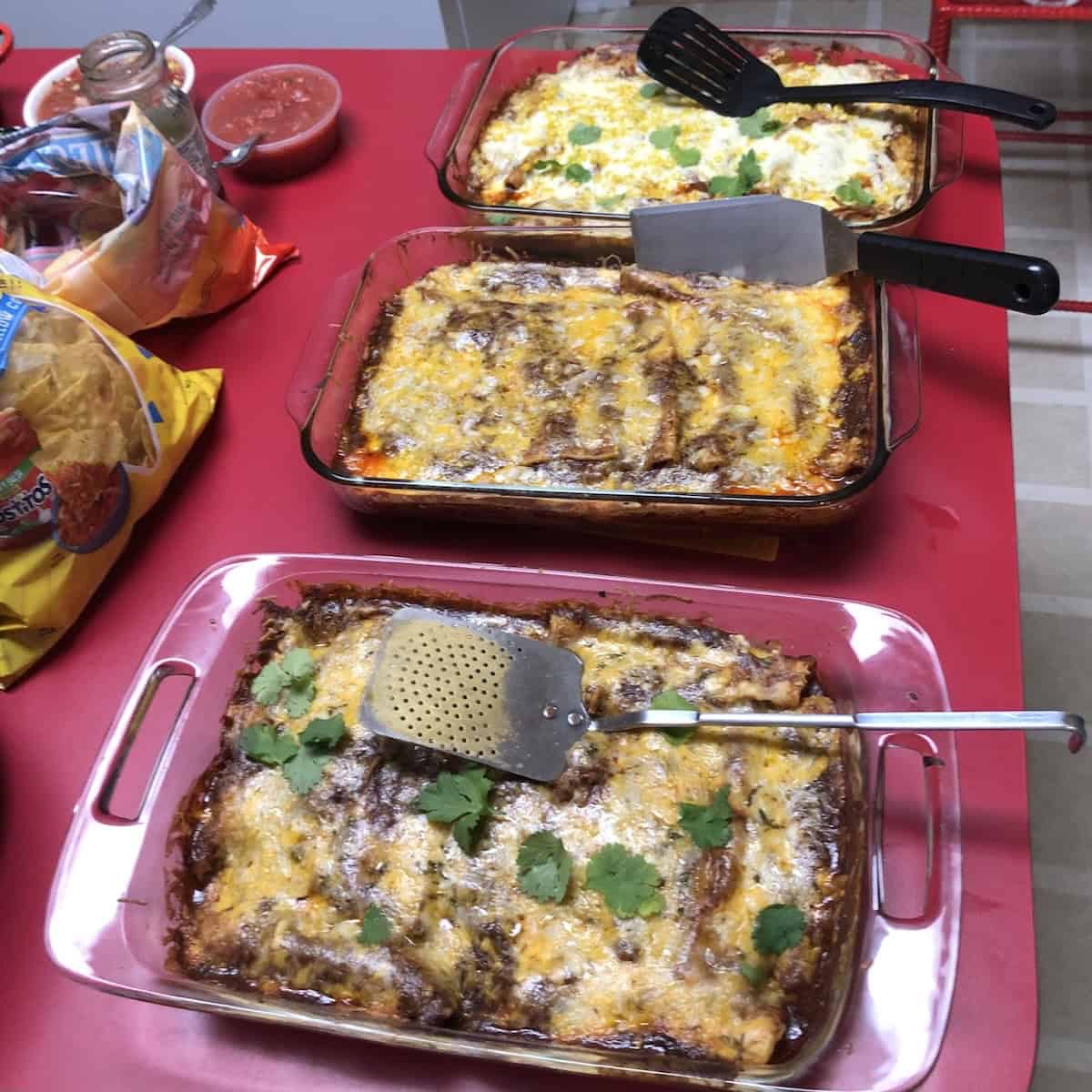 Pre-Thanksgiving meal at my sister's house with 3 different 9x13 inch pyrex glass casserole dishes filled with cheese enchiladas, shredded pork enchiladas, and cheese enchiladas with tortilla chips and salsa in the background.