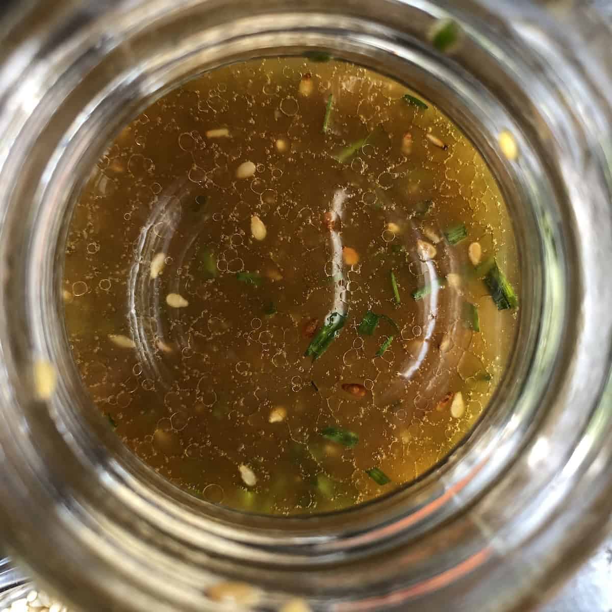 Homemade Asian sesame dressing in a small Weck Canning jar with toasted sesame seeds and fresh chives floating on top, showcasing its rich amber color and smooth texture.