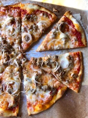 Sliced cheesy thin-crust pizza topped with homemade sausage and onions.