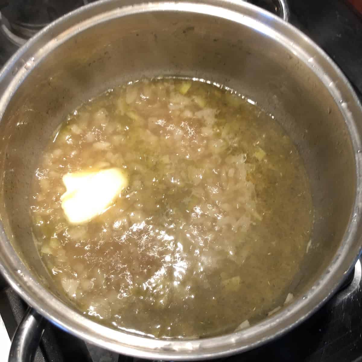Chicken stock added to the aromatics and brought to a boil then the butter is added which is a crucial step in preparing authentic Italian Mediterranean vegetable couscous before adding the dry couscous to absorb the flavorful liquid.
