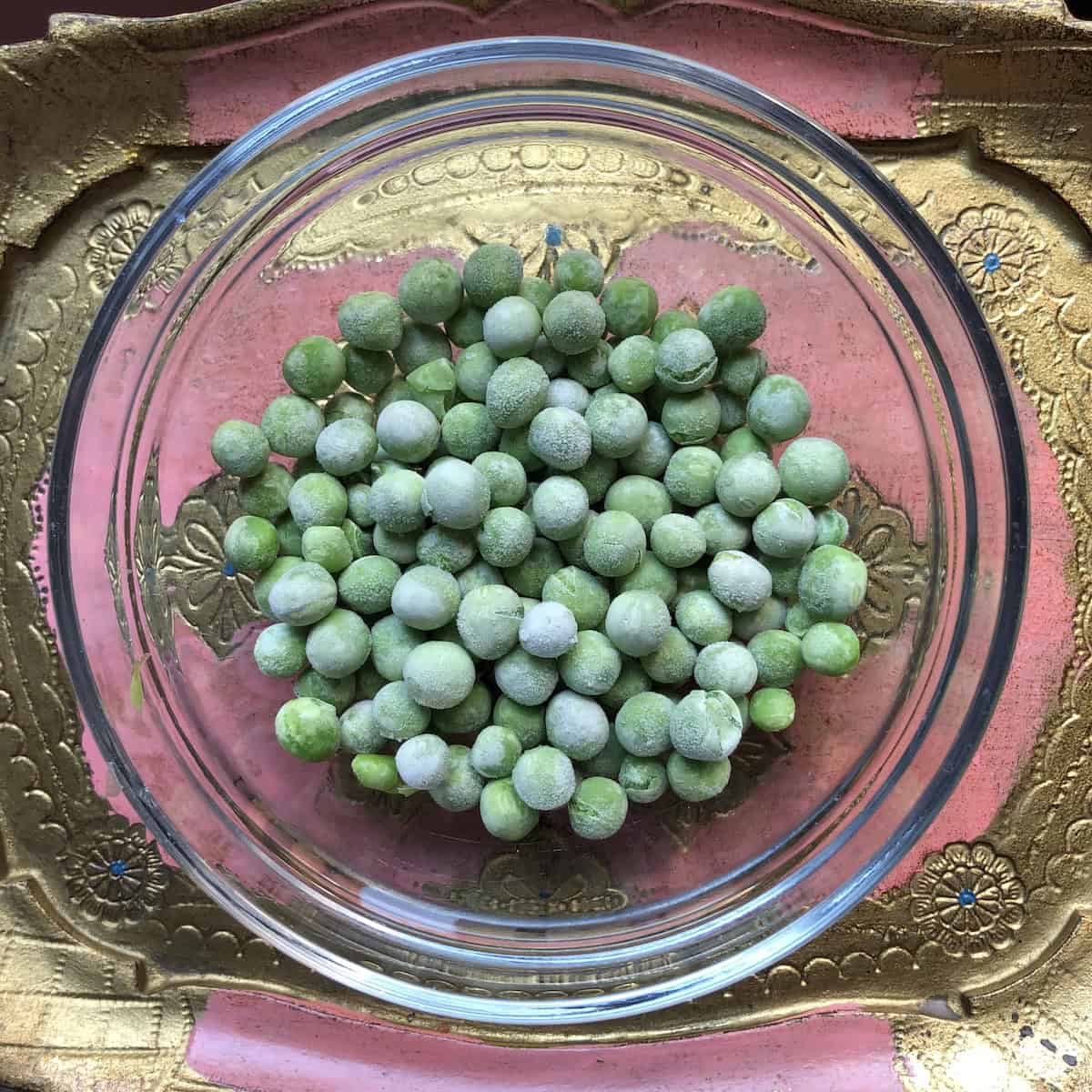 Frozen peas with icy appearance in a small prep bowl for authentic Italian Mediterranean vegetable couscous recipe, showing ingredients before soaking in water for a few minutes and draining as required for proper texture in homemade couscous.