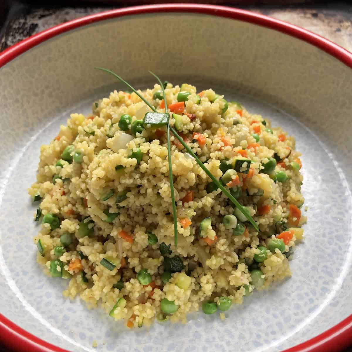 Close-up of perfectly prepared homemade Italian Mediterranean vegetable couscous garnished with fresh chives, showing the superior texture and authentic flavor achieved through proper cooking techniques that rivals artisanal store-bought versions at a fraction of the cost.