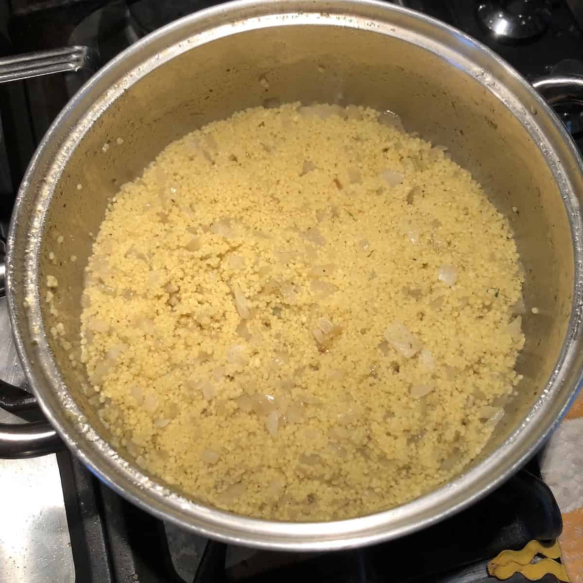 Perfectly steamed Italian Mediterranean couscous that has rested covered for exactly 7 minutes, showing the ideal fluffy texture achieved through proper cooking technique before combining with caramelized vegetables for an authentic homemade vegetable couscous recipe.