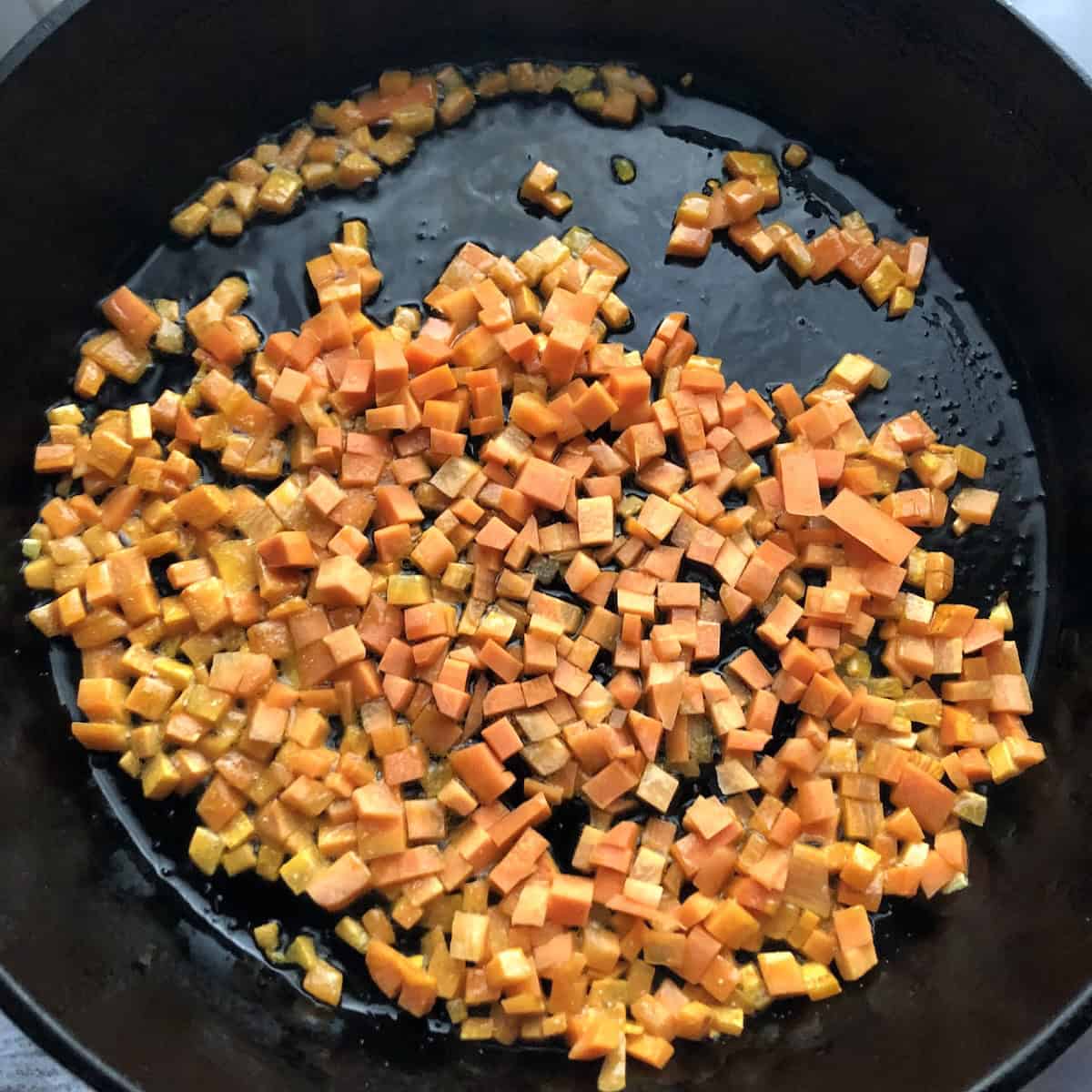 Finely diced carrots caramelizing in extra virgin olive oil in a cast iron skillet for couscous, building depth of flavor through proper vegetable preparation and layering techniques.