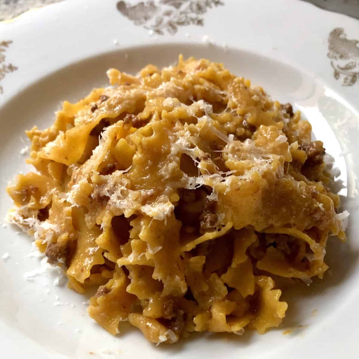 Pumpkin tagliatelle pasta with authentic bolognese meat sauce ragu in a pasta bowl sprinkled with grated Grana Padano. 