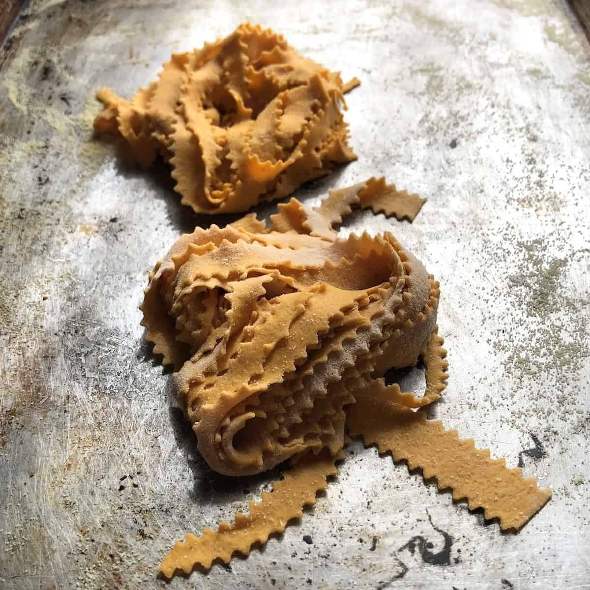 Homemade pumpkin fettuccine pasta nests on semolina dusted baking tray ready to cook or freeze, fresh pumpkin pasta recipe.