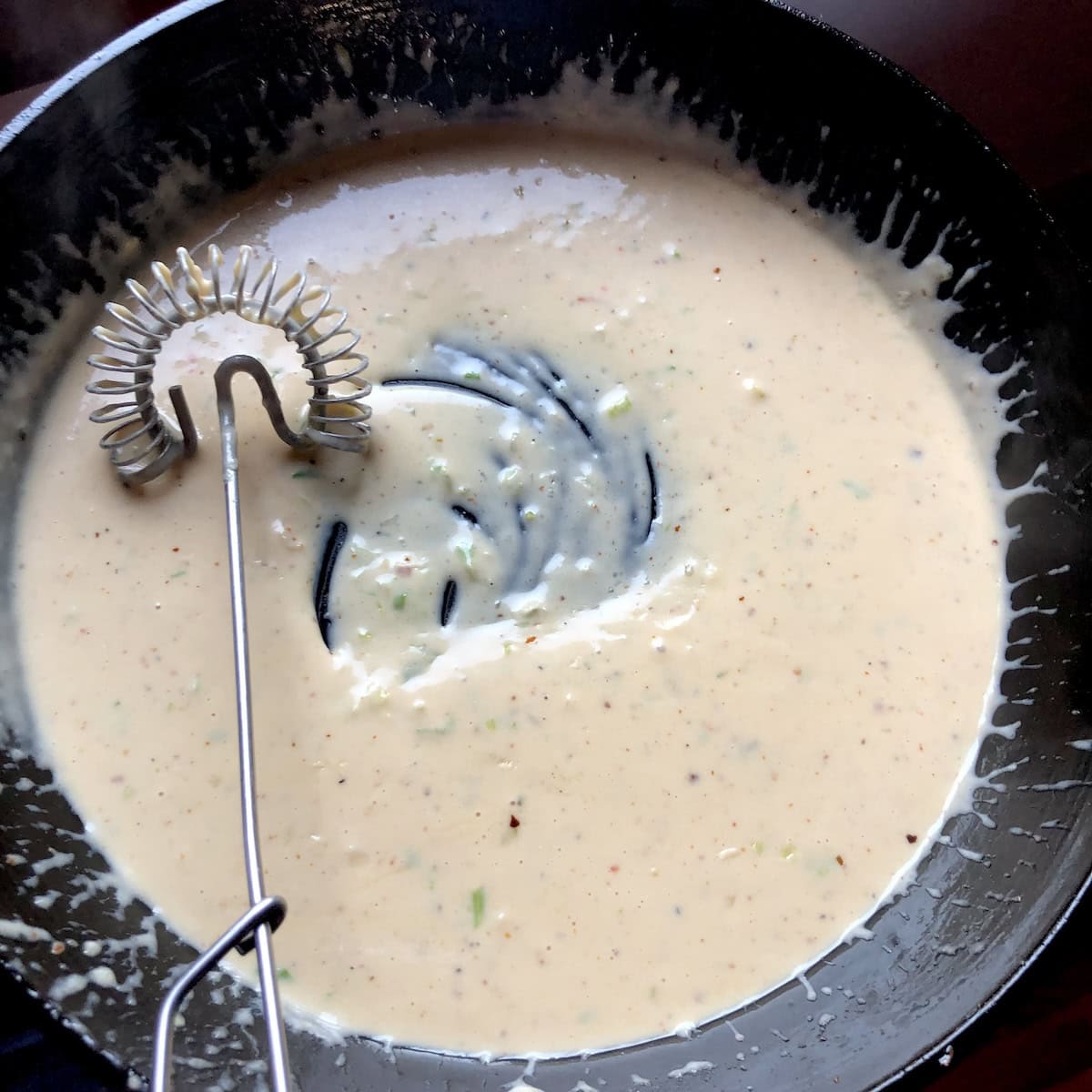Homemade alfredo sauce in skillet with flat whisk, creamy white pasta sauce recipe for fresh homemade pasta.