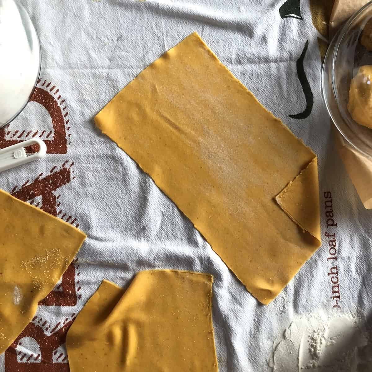 Fresh pumpkin lasagna noodles cut to size on tea towel for homemade pasta recipes for Halloween or Fall.

