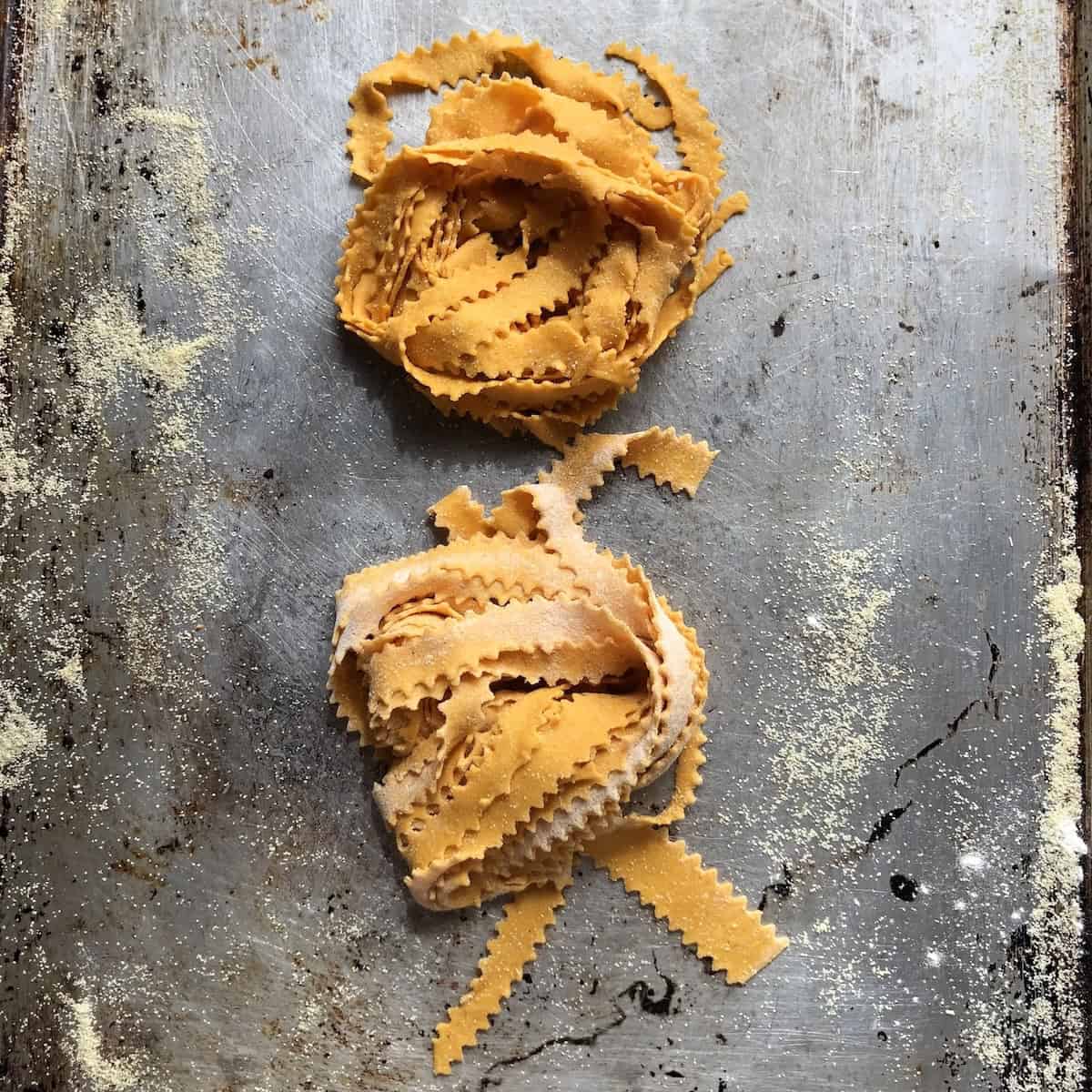 Homemade pumpkin pasta recipe reginelle noodles in nests on semolina dusted tray, (fresh pumpkin fettuccine pasta) with zigzag edges ready to cook or freeze for easy pumpkin recipes.