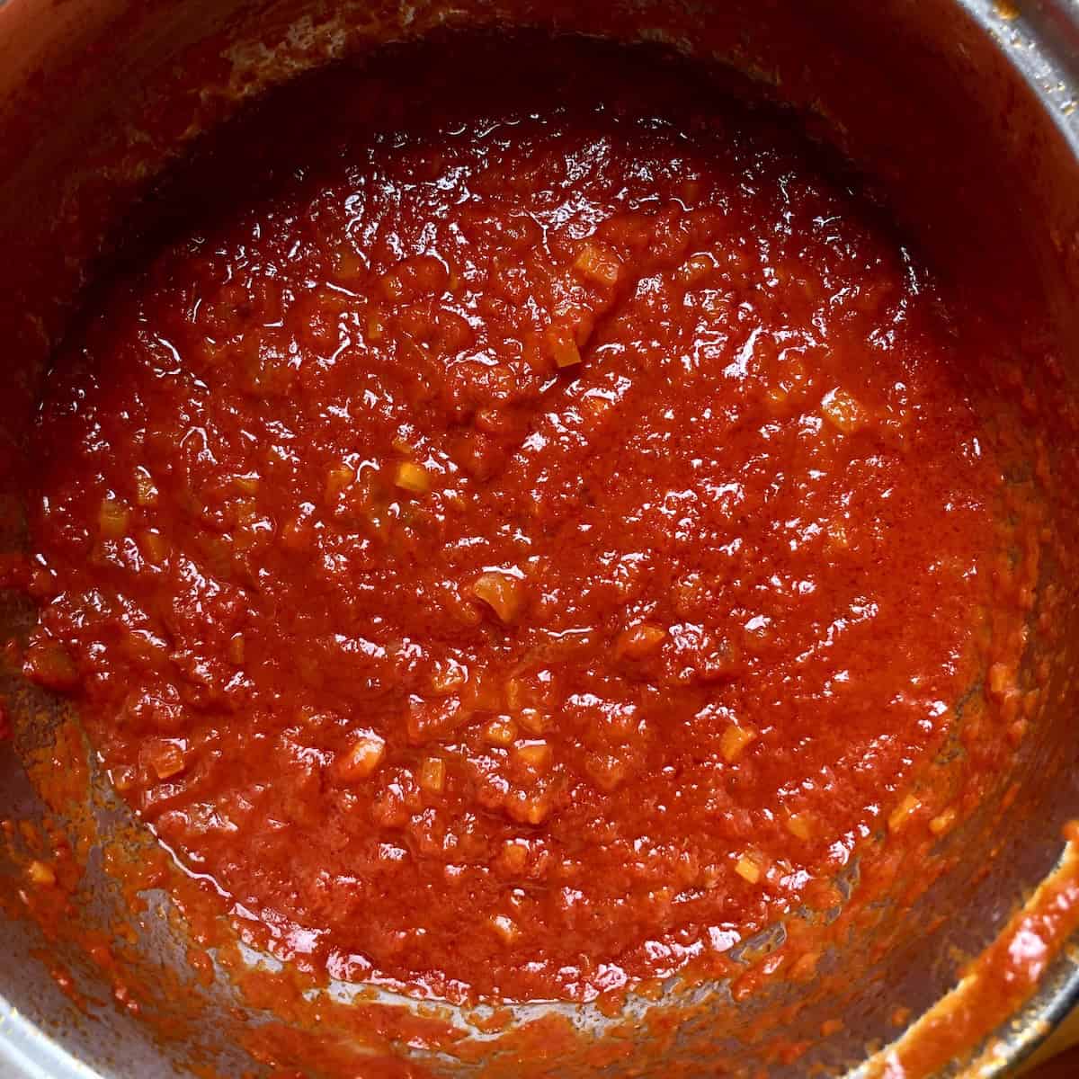 Homemade tomato sauce with Italian tomatoes in stainless steel pot, classic Italian marinara pasta sauce recipe from scratch.