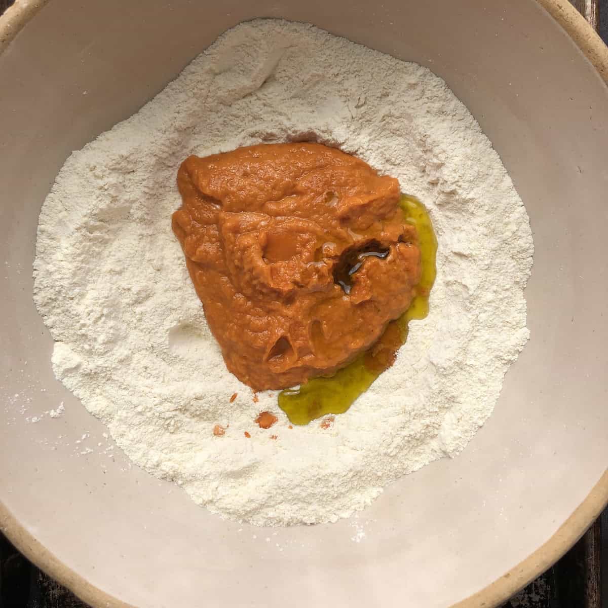 Pumpkin puree mixture and extra virgin olive oil added to the flour well not yet mixed in. 
