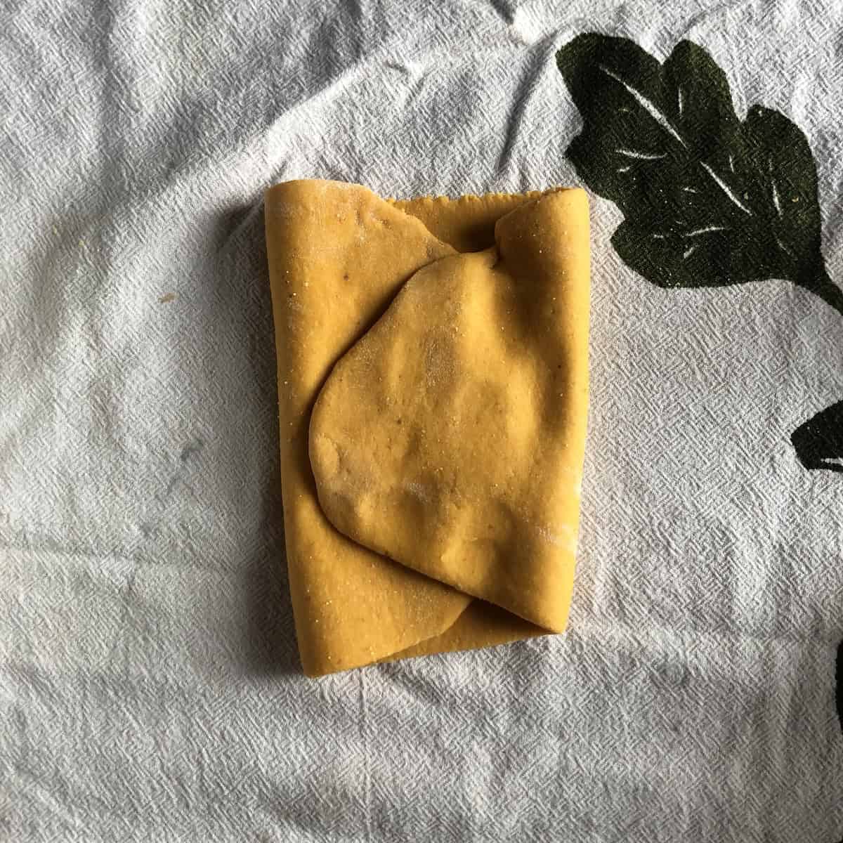 Sheeted pumpkin pasta dough folded into thirds  to create a more uniform rectangular piece before rolling out.
