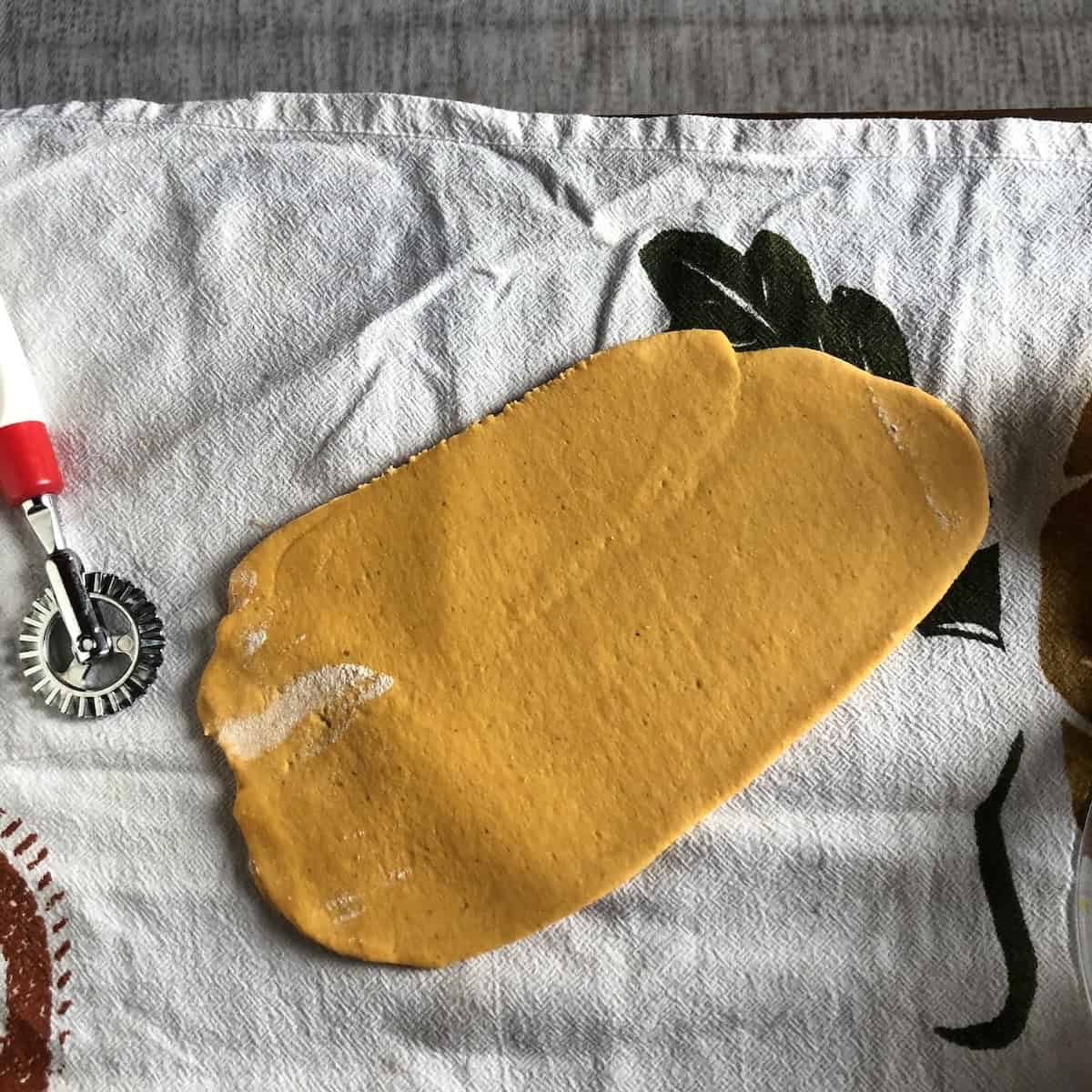 Rolling pumpkin pasta through pasta machine widest setting to create uniform sheet for rolling out into consecutively thinner sheets. 