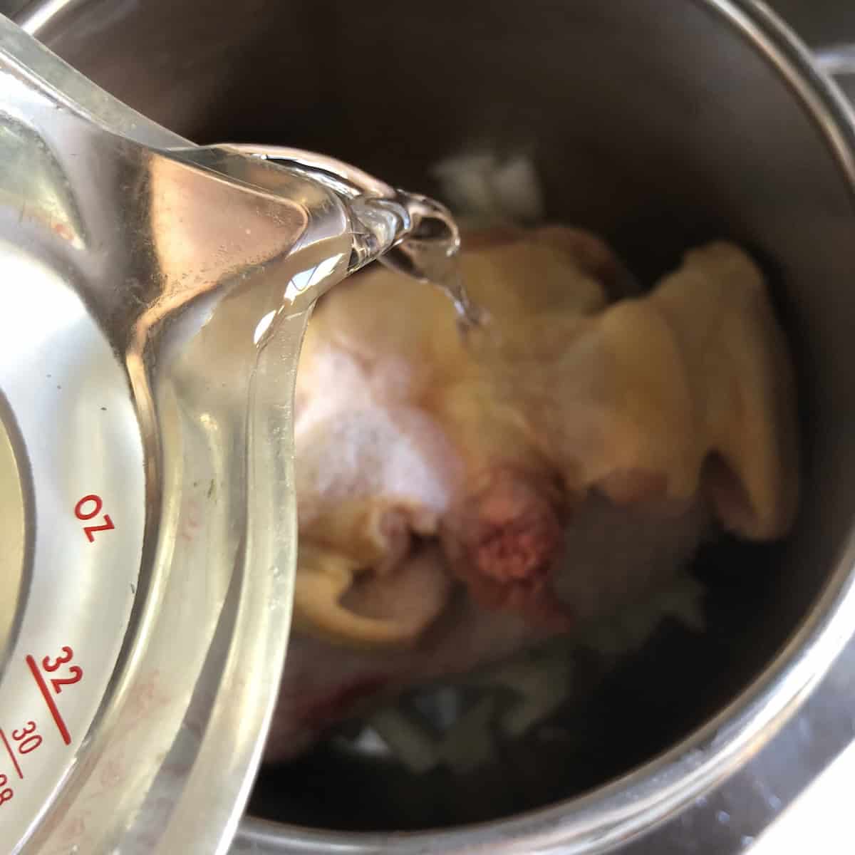 Adding water to chicken bones, vegetables, and aromatics in pressure cooker for making homemade chicken broth recipe showing how to make chicken broth step.
