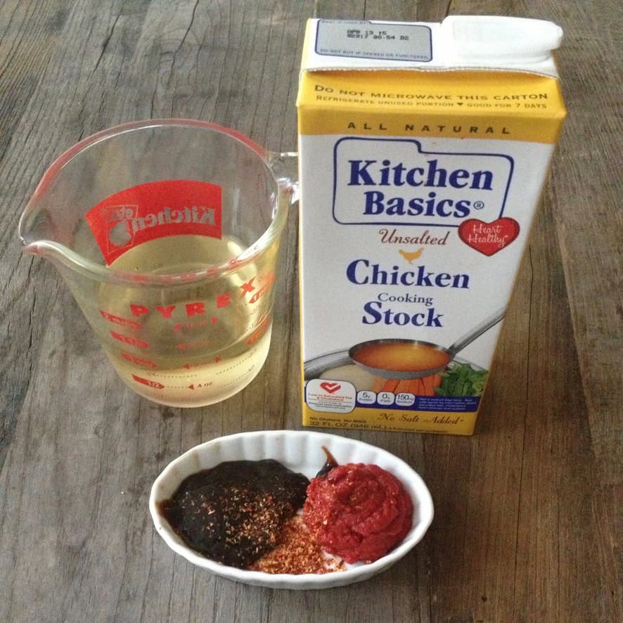 Kitchen Basics all-natural unsalted chicken broth carton with fresh ingredients for making a recipe at home using boxed stock instead of homemade.
