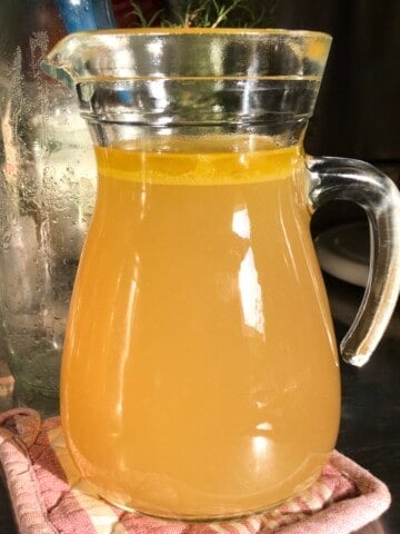Homemade chicken broth with rich golden color in a clear glass pitcher looking nothing like bland storebought chicken broth.