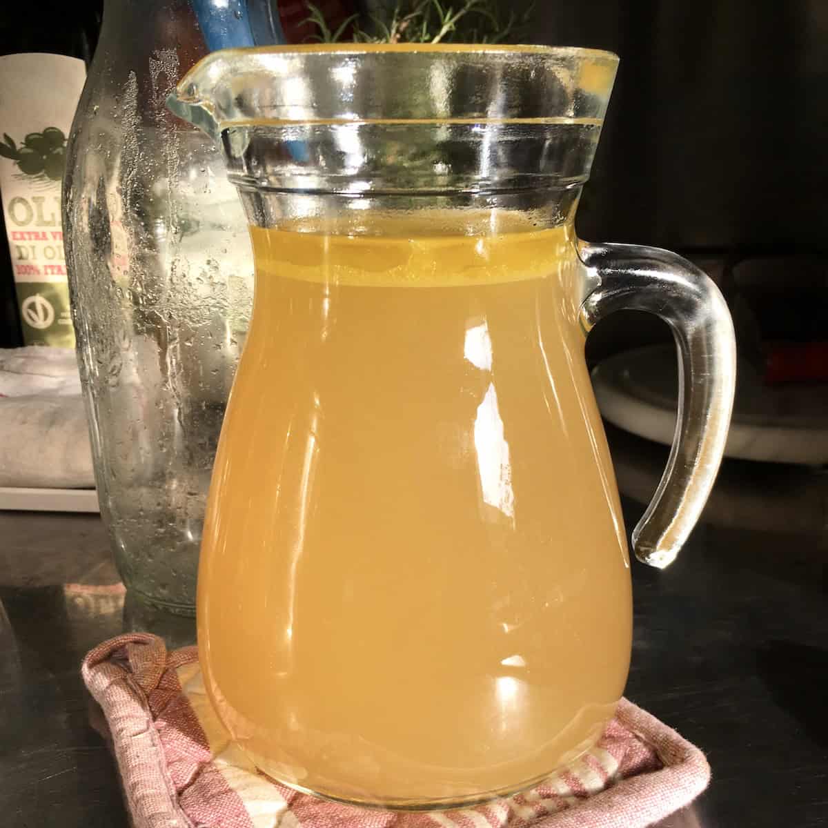 Homemade chicken broth with rich golden color in a clear glass pitcher looking nothing like bland storebought chicken broth.