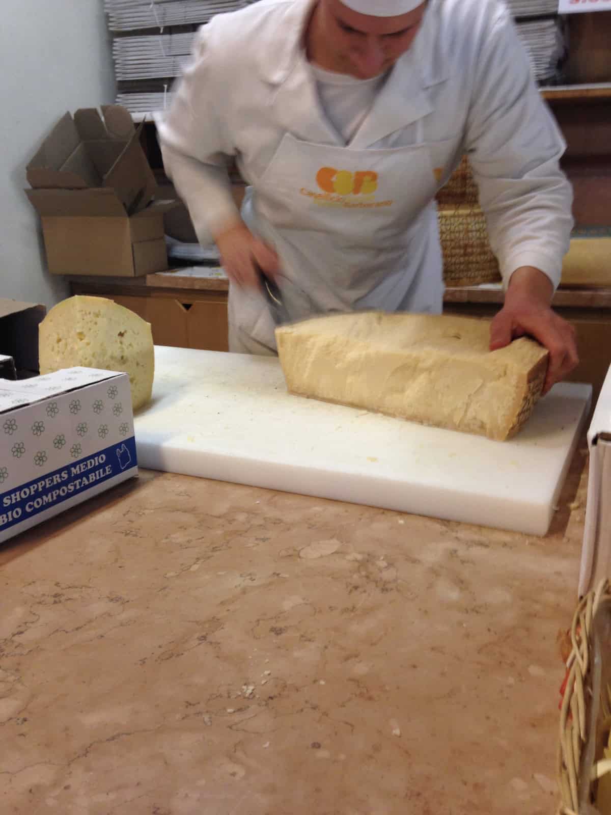 Northern Italian caseficio in Barbarano showing our cheesemonger cutting aged grana padano wheels for our wedges and trimming off some of the rinds before weighing and charging us for the cheese (then giving me a bag full of cheese rinds for my homemade chicken broth recipe secret ingredient.