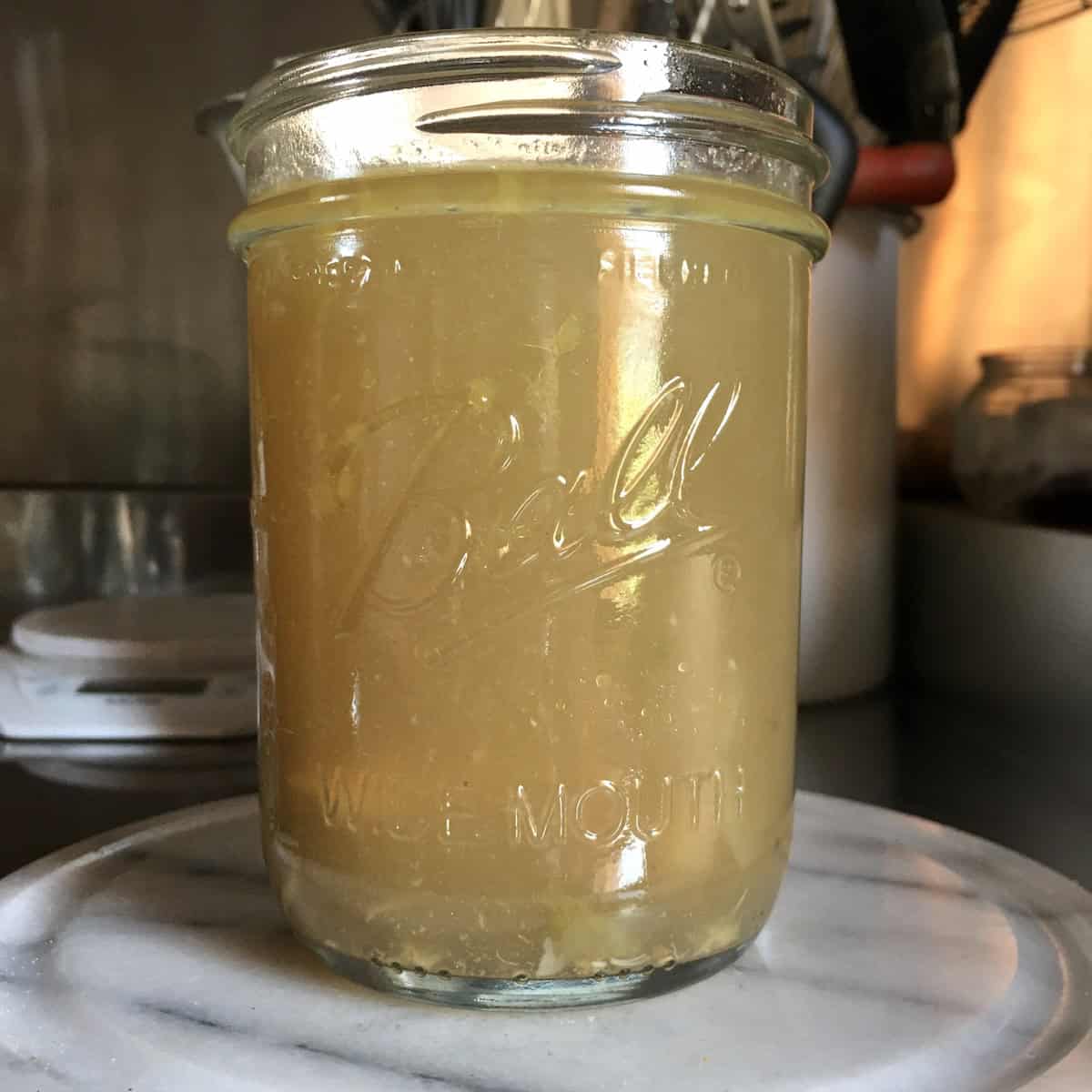 Homemade chicken broth in wide mouth Ball canning pint jar showing cloudy appearance from quick release pressure cooker method for how to make chicken broth.