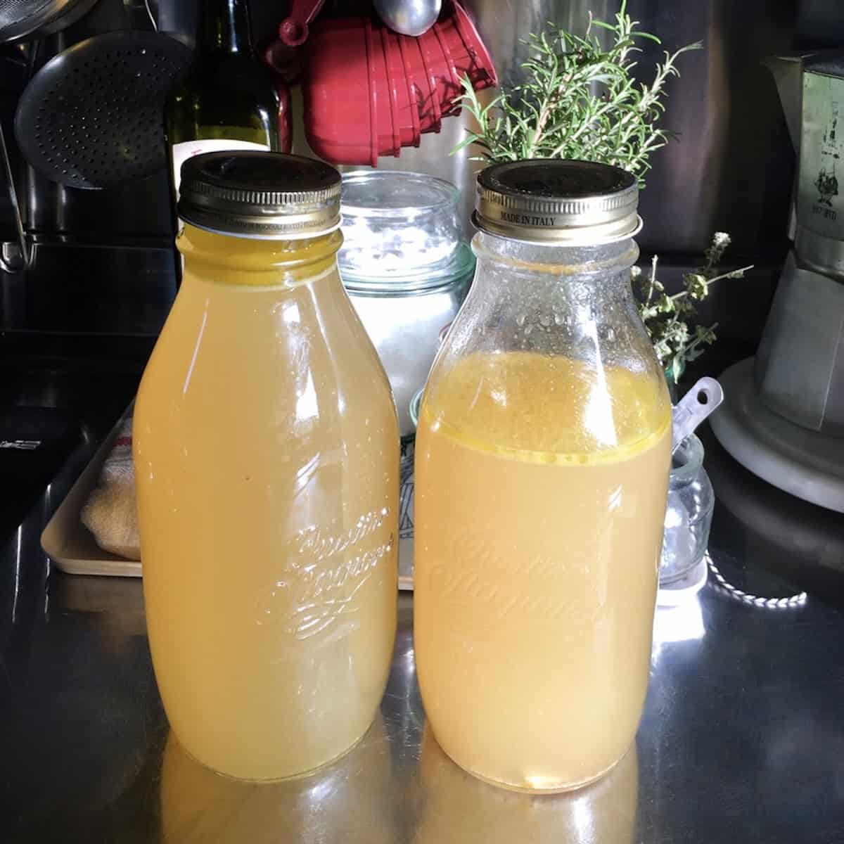 Two glass jars filled with golden homemade chicken broth showing a visible layer of fat on top ready to refrigerate (shows the easiest way to skim the fat from homemade chicken broth).