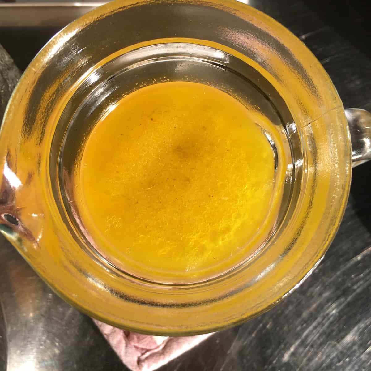 Top down view of homemade chicken broth in glass pitcher showing golden schmaltz chicken fat layer risen to the top for easy removal after refrigeration.

