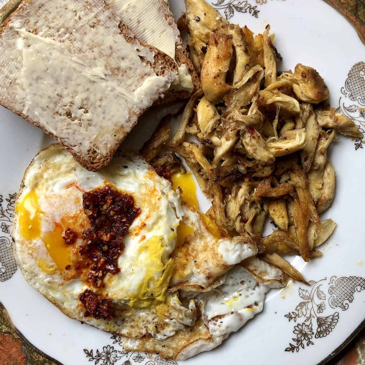 A plate with breakfast featuring eggs over medium, buttered wheat toast, and spent chicken leftover from making chicken broth turned into delicious chicken breakfast "sausage". 
