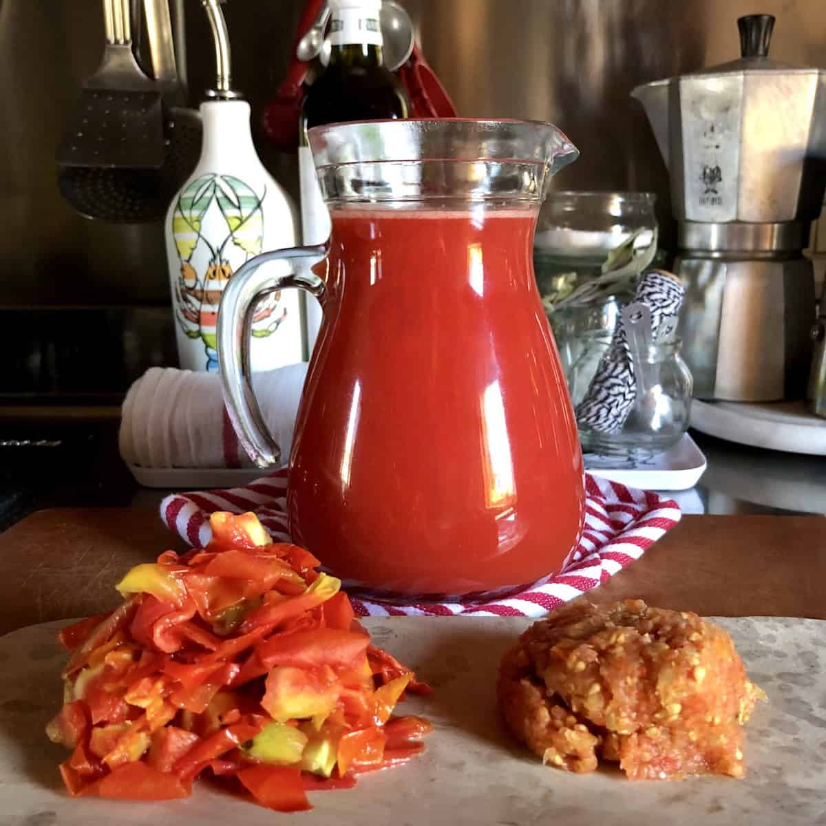 Glass pitcher of homemade tomato passata with tomato seeds and skins in separate piles on platter showing zero waste kitchen ingredients saved for homemade chicken broth recipe.

