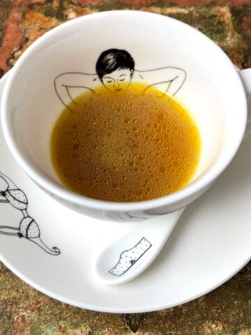 Anti-inflammatory turmeric ginger mushroom chicken bone broth in ceramic mug showing healing sippable golden broth with health benefits for wellness.