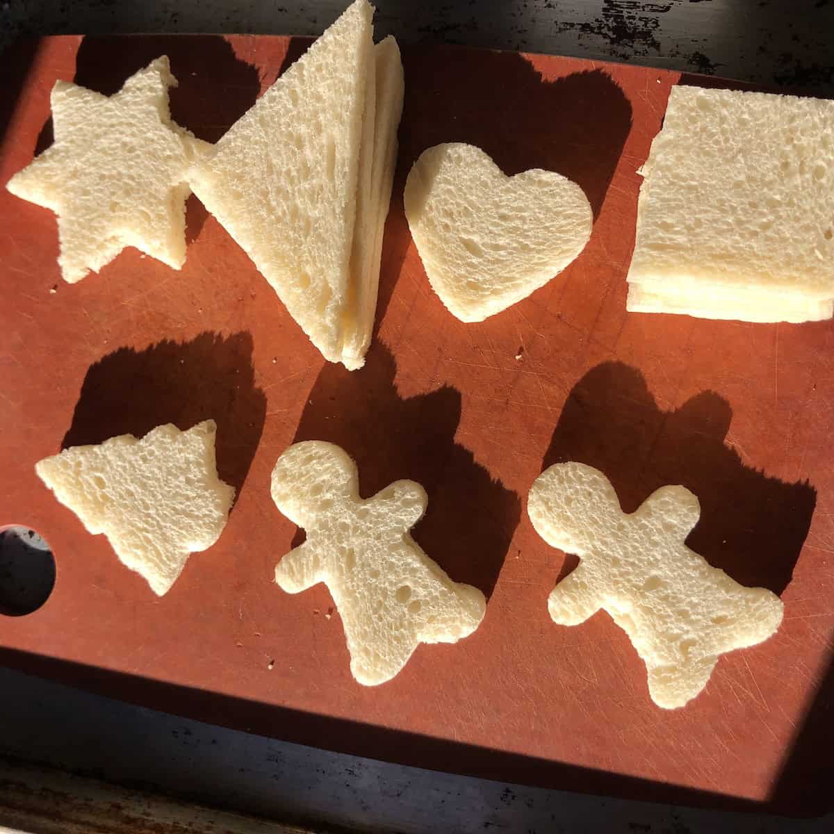 Crustless white sandwich bread cut into holiday shapes including Christmas trees, gingerbread men, stars, and hearts for Valentines day shrimp toast (or Mother's Day Shrimp toast) and regular squares and triangles showing the best bread too use for shrimp toast and how you can cut them.
